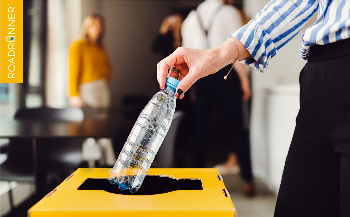 A woman in an office placing a plastic bottle in a recycling bin.