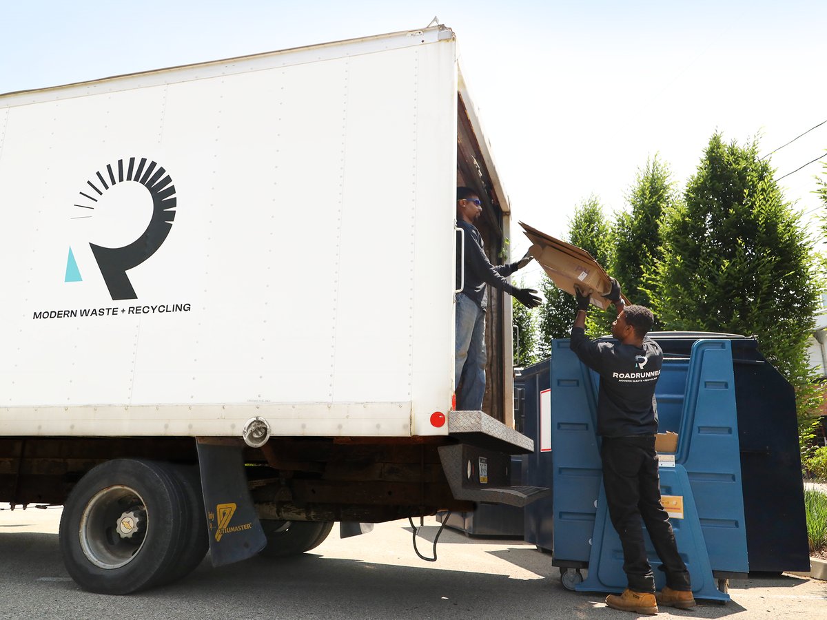 two people putting cardboard from a crate into a box truck