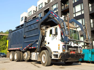 A front-load dumpster truck in front of an apartment complex.