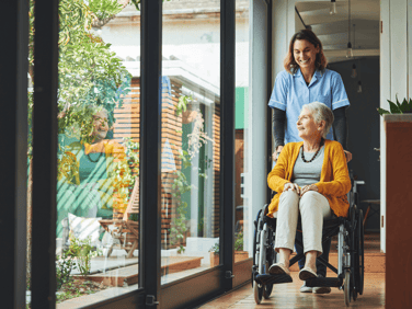 Interior of a healthcare facility with a nurse pushing an elderly woman in a wheel chair