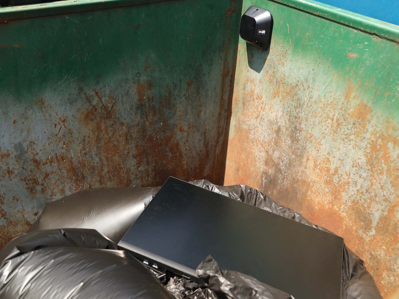 a trash dumpster filled with garbage bags and a computer monitor