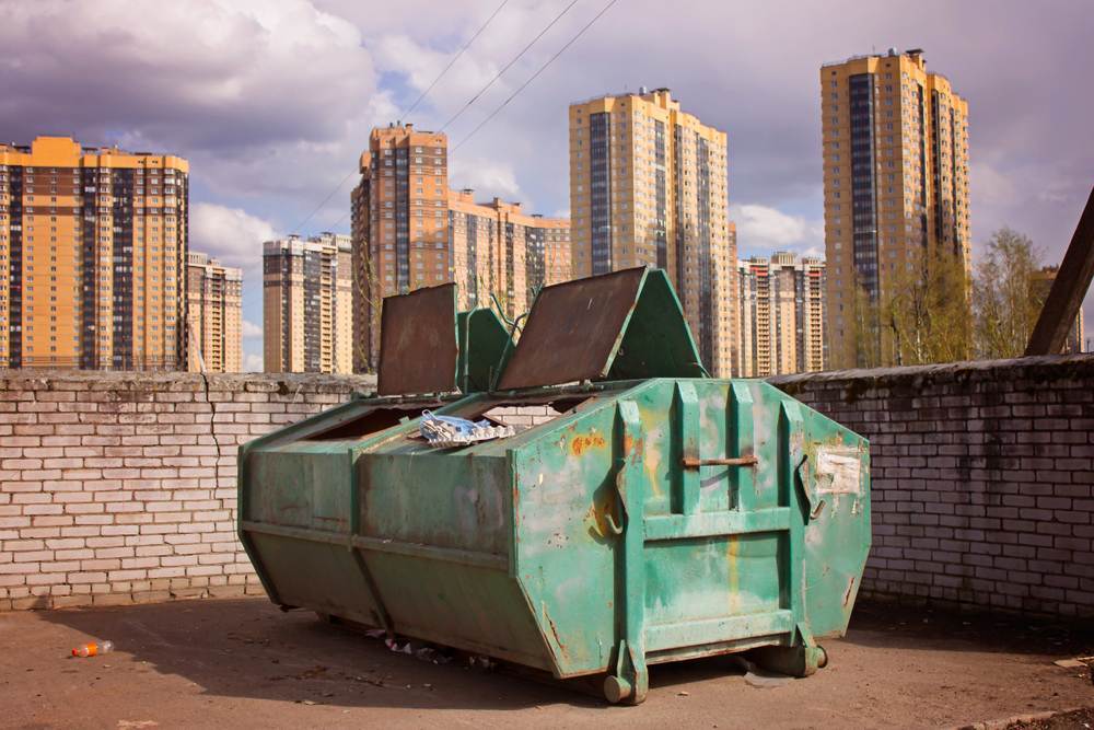 Green garbage container with high-rise buildings on the background