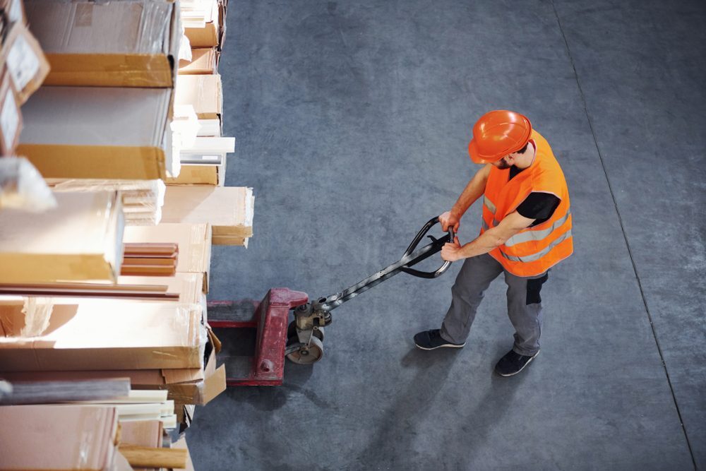 Top view of young male worker in uniform that is in the warehouse moving cardboard.