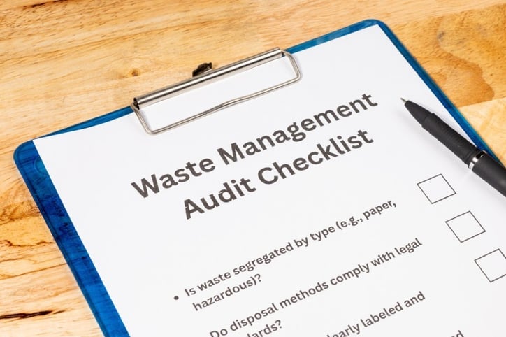 A waste management audit checklist is held by a clipboard in a close-up view.