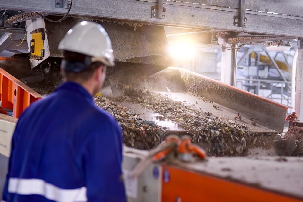 A worker watching industrial waste coming down a chute into a facility.