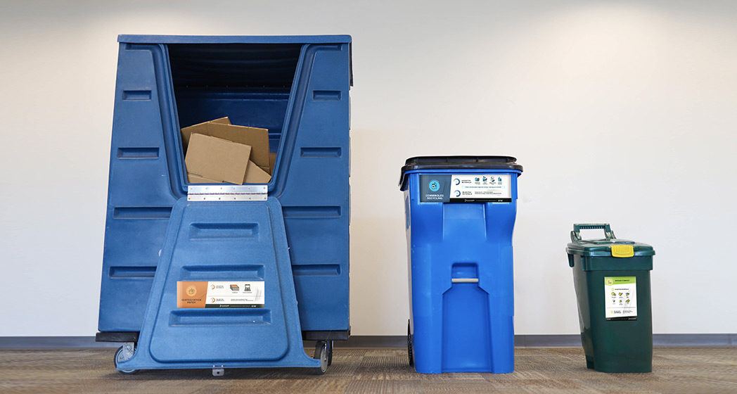 three trash containers in a room with cardboard, plastic and glass recycling, and composting